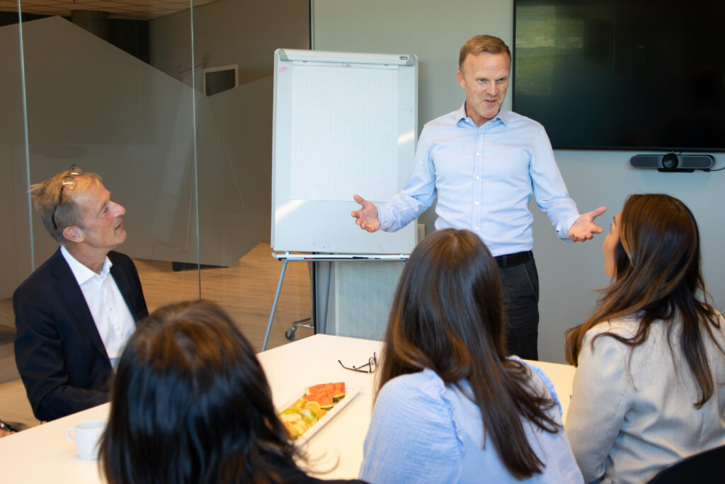En kursholder står og snakker foran en gruppe mennesker på et salgstreningskurs.